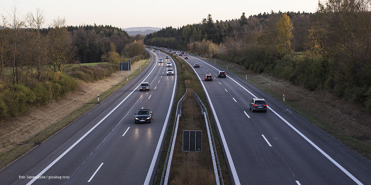 KI generiert: Das Bild zeigt eine Autobahn mit zwei Richtungsfahrbahnen, auf der mehrere Autos unterwegs sind. Die Umgebung besteht aus Bäumen und ist von Natur umgeben.