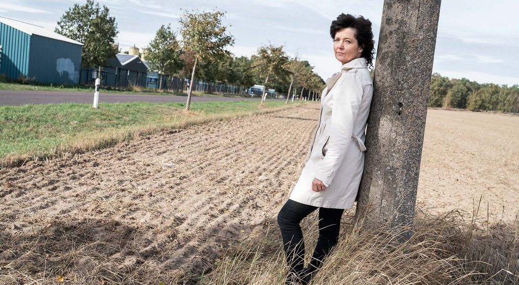 Petra Hennigs lehnt an einem Pfeiler, der sich auf einem Acker und neben einer Straße befindet.