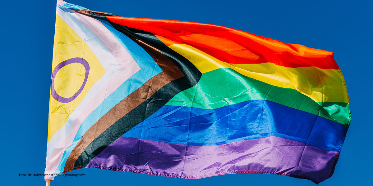 KI generiert: Das Bild zeigt eine inklusive Pride-Flagge, die im Wind weht. Die Flagge kombiniert die traditionellen Regenbogenfarben mit zusätzlichen Streifen in anderen Farben, um verschiedene Identitäten zu repräsentieren.
