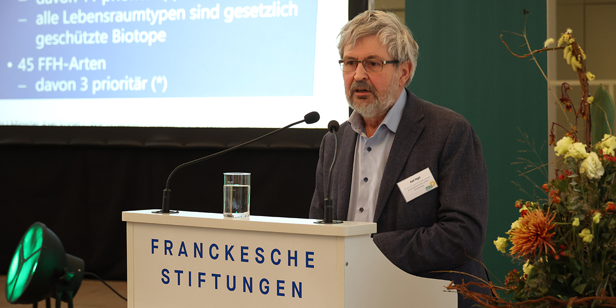 KI generiert: Eine Person steht am Rednerpult und spricht, während im Hintergrund eine Präsentation zum Thema Biotop- und Artenschutz projiziert wird. Das Rednerpult trägt die Aufschrift "Franckesche Stiftungen".