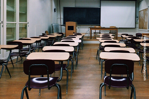 Ein leeres Klassenzimmer mit Stizbänken, Tafel, Rednerpult und Leinwand.