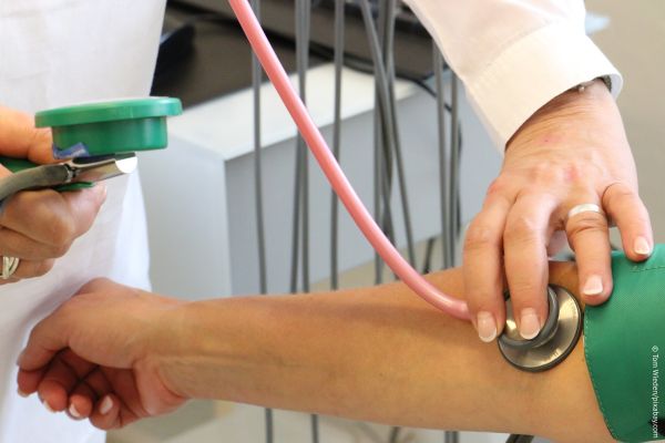 KI generiert: Ein Arzt misst den Blutdruck mithilfe eines Stethoskops und einer Blutdruckmanschette am Arm eines Patienten. Hauptinhalt des Bildes ist die medizinische Untersuchung.