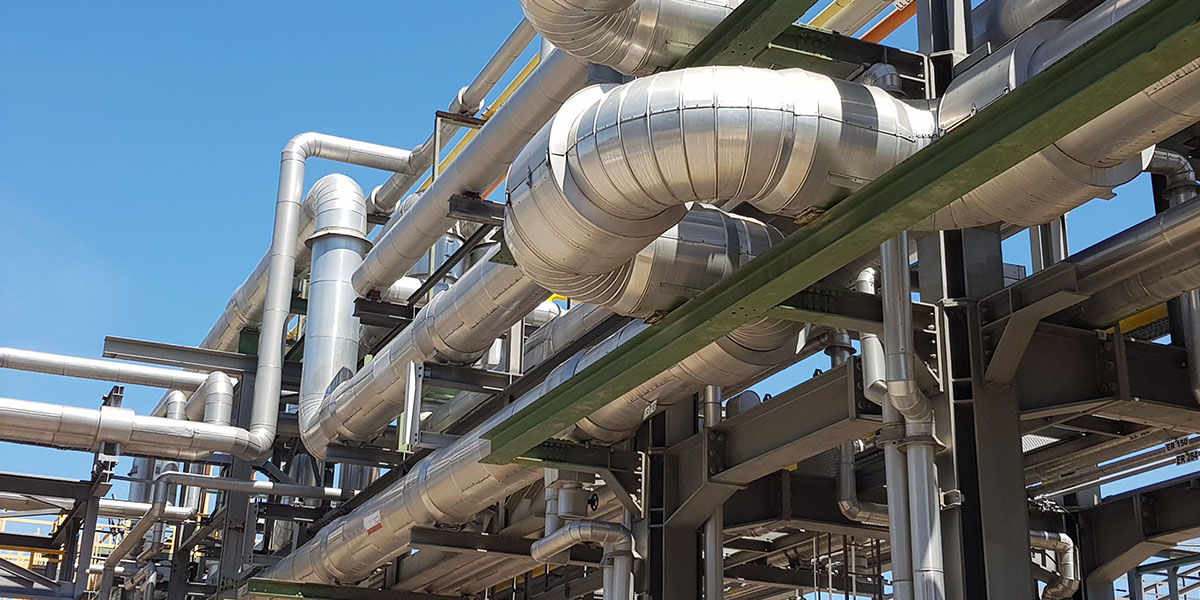 KI generiert: Das Bild zeigt eine komplexe Anordnung von metallischen Rohren und Leitungen in einem industriellen Umfeld. Diese sind in einem tragenden Gerüst aus Stahl eingebettet und verlaufen in verschiedene Richtungen unter freiem Himmel.