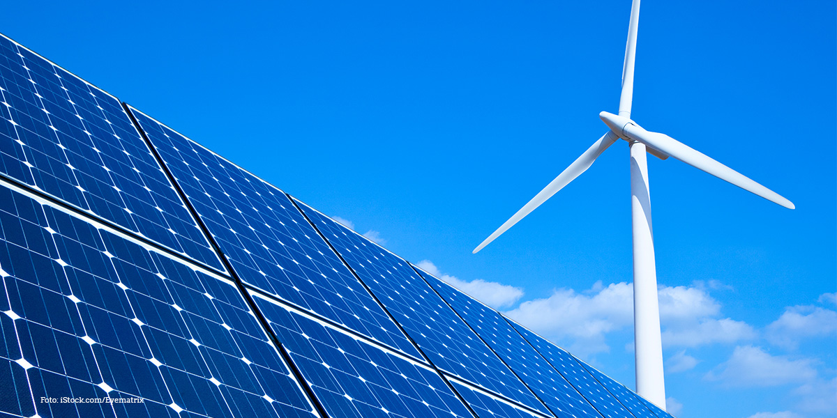 KI generiert: Das Bild zeigt Solarpaneele im Vordergrund und ein Windrad im Hintergrund unter klarem, blauem Himmel. Der Hauptinhalt des Bildes sind erneuerbare Energien.