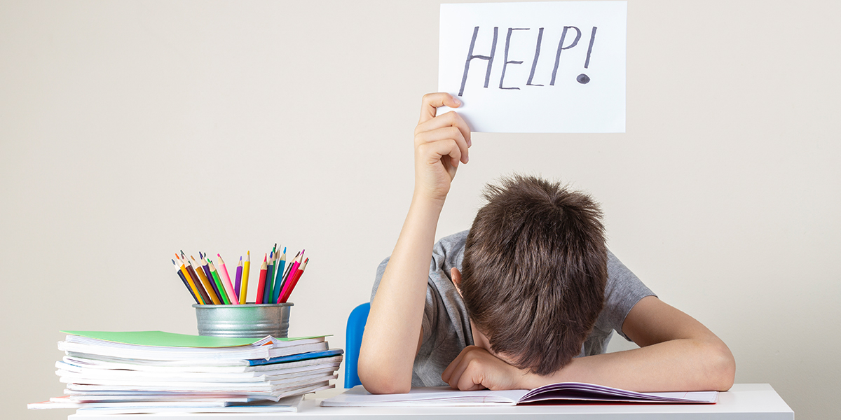 KI generiert: Das Bild zeigt ein Kind, das mit dem Kopf auf einem Tisch liegt und ein Blatt Papier mit der Aufschrift "HELP!" hochhält. Auf dem Tisch befinden sich ein Haufen Bücher und ein Becher mit Buntstiften, was auf eine Überforderung oder Frustration im Zusammenhang mit Hausaufgaben hindeuten könnte.