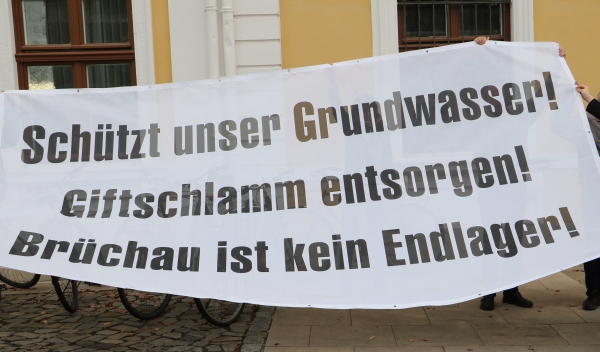 KI generiert: Das Bild zeigt ein Banner mit der Aufschrift "Schützt unser Grundwasser! Giftschlamm entsorgen! Brüchau ist kein Endlager!" Dies weist auf einen Protest gegen die Entsorgung von Giftschlamm und die Nutzung von Brüchau als Endlager hin.