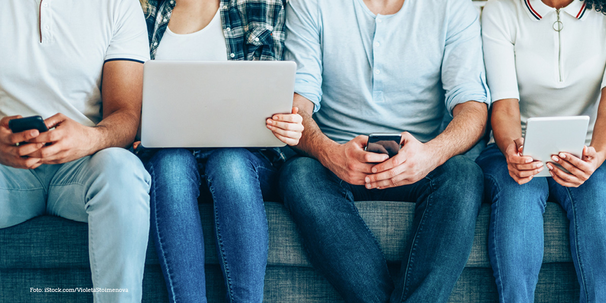 Menschen sitzen auf einem Sofa und bedienen technische Geräte. 